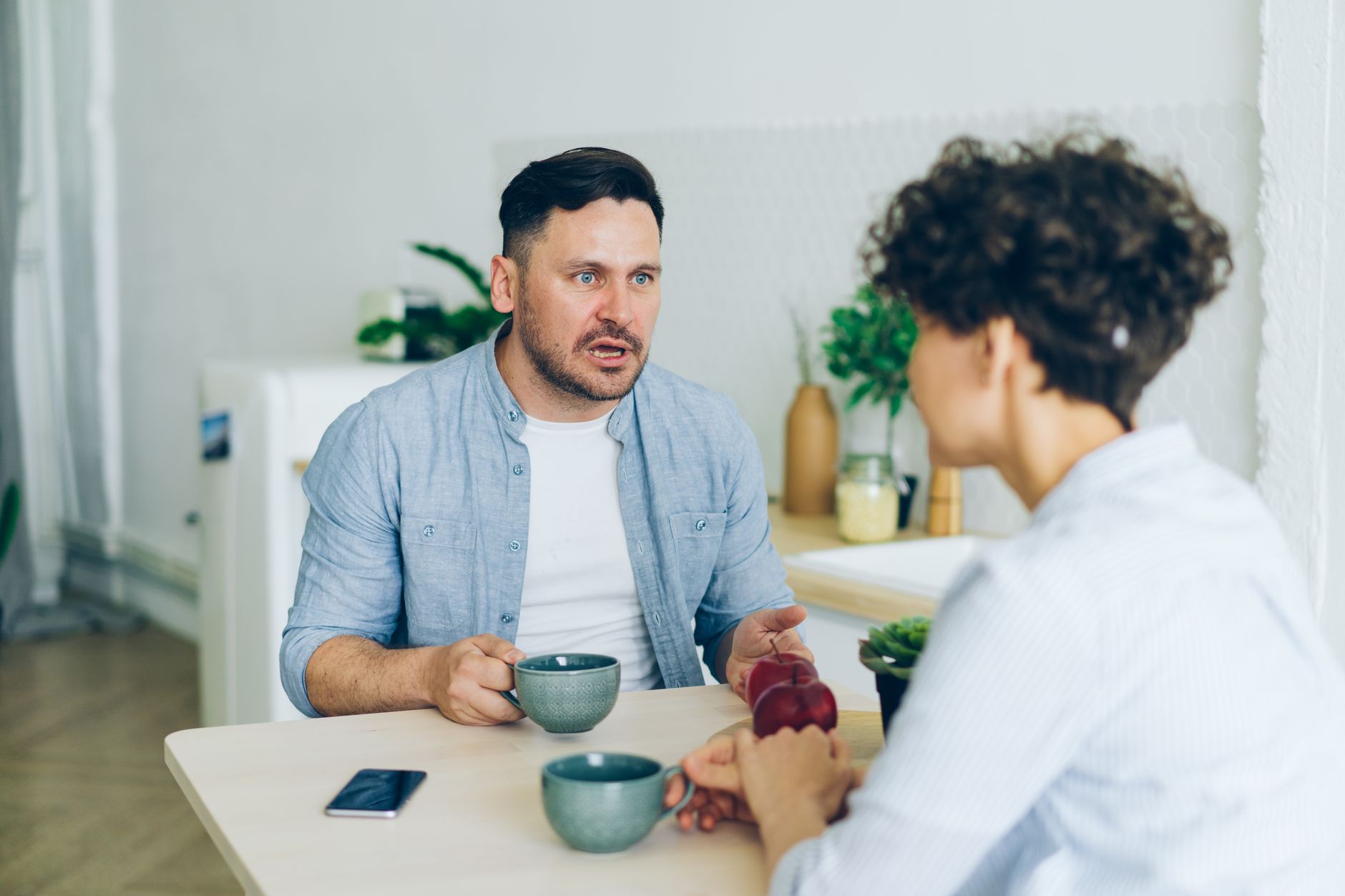 Stel voert een gespannen gesprek aan de keukentafel met koffiekopjes voor zich