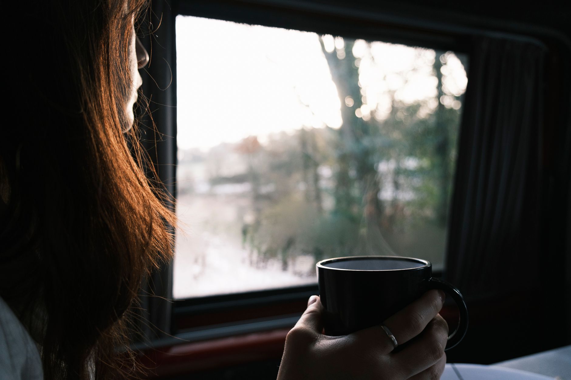 Vrouw met een mok koffie in haar hand kijkt naar buiten door het raam